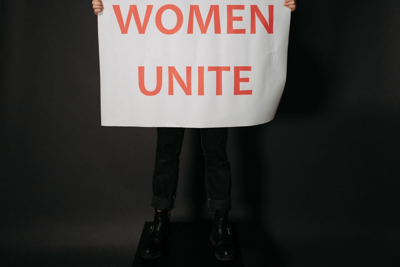 Studio shot of hands holding a Women Unite poster against a black background, symbolizing empowerment.